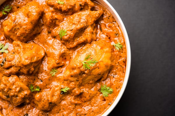 A close-up of a rich, creamy Instant Pot butter chicken in a white bowl against a dark background