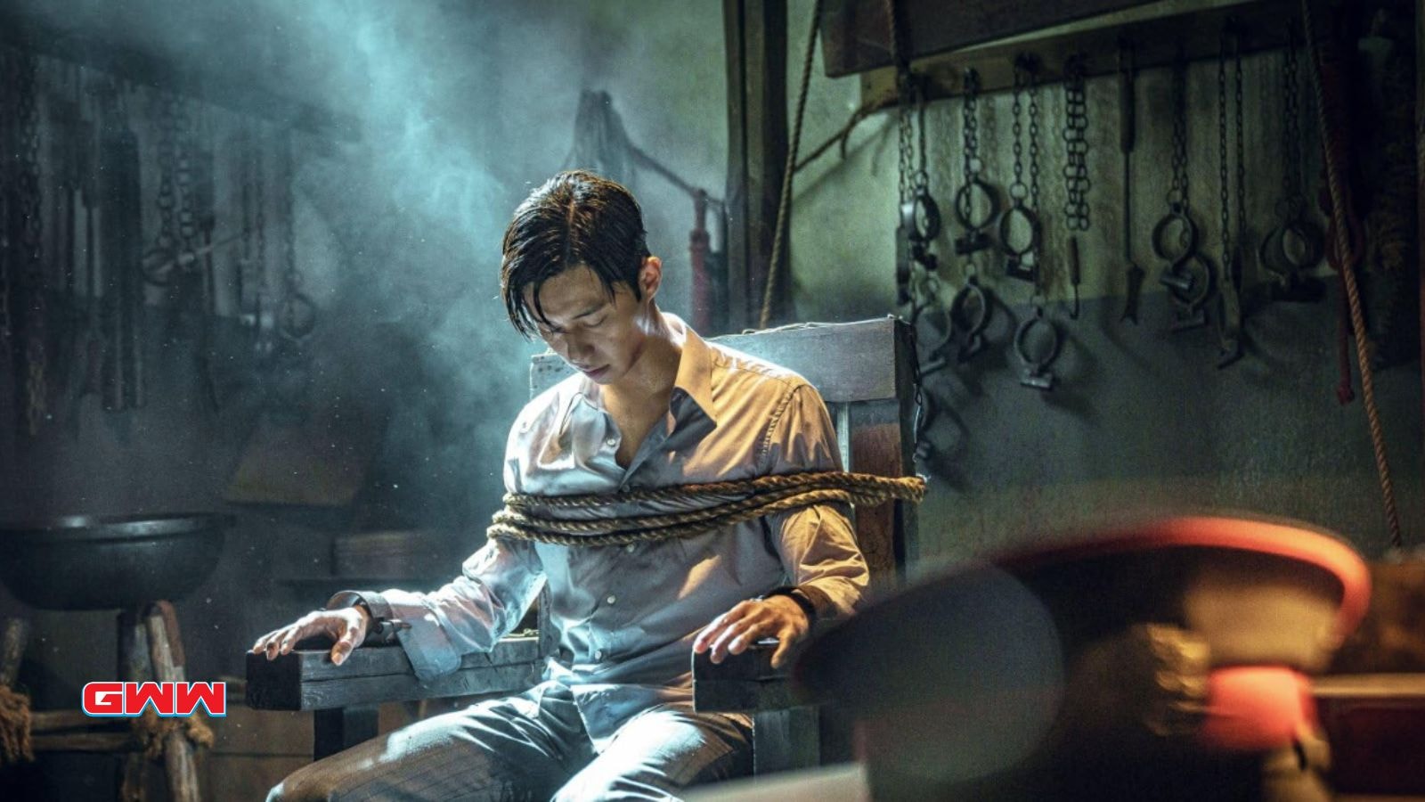 Jang Tae-sang tied to a chair in a dimly lit, eerie torture room.