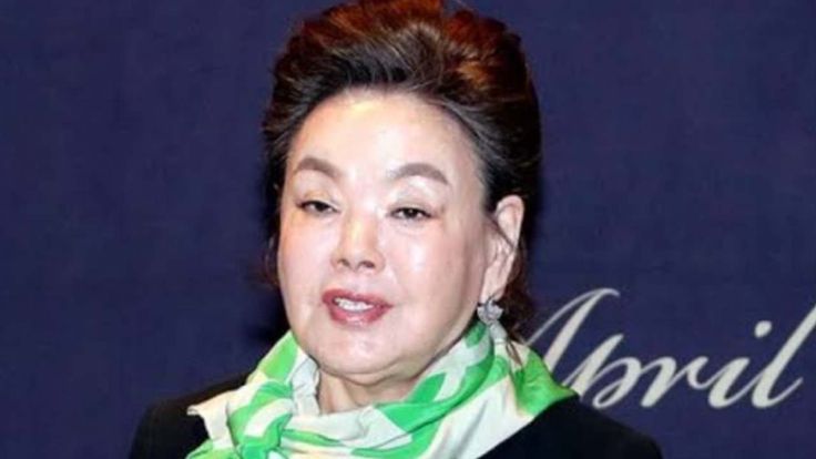 A picture of Veteran actress Kim Soo Mi on a green and white scafe  on her neck putting on a black jeacket