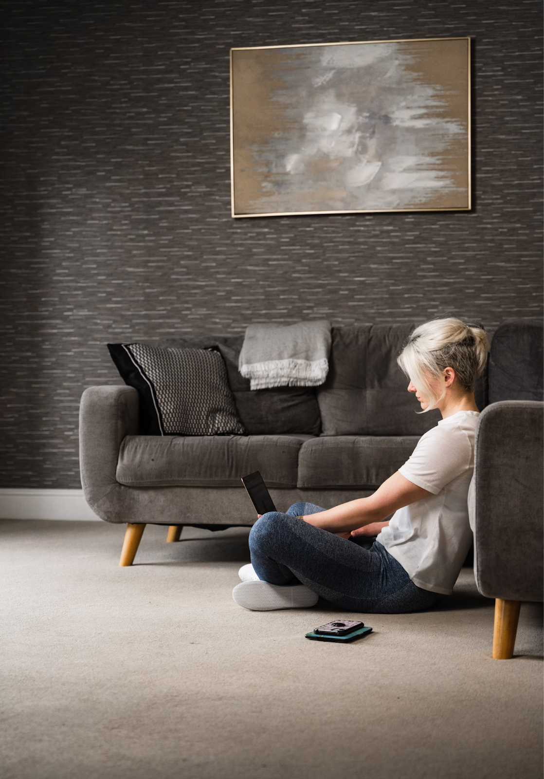 A woman sits cross-legged in her living room with her back against the sofa. She has her laptop balanced on her knee as she looks up how to cite websites in MLA.