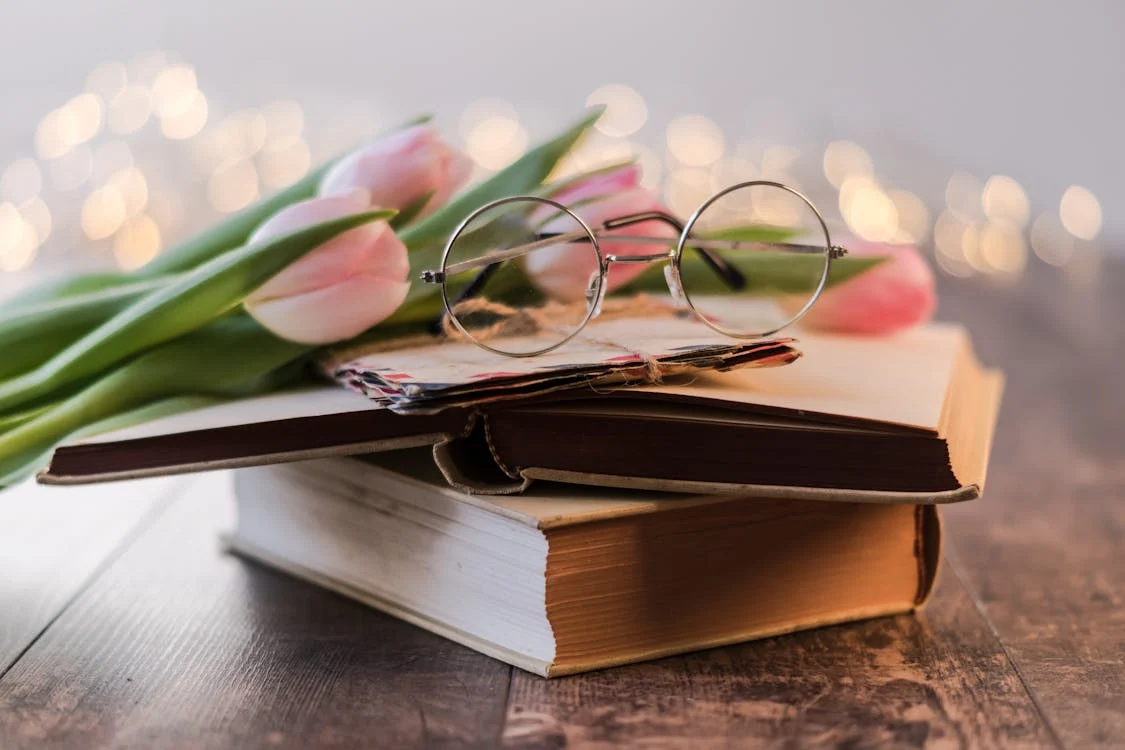 books stacked with pink tulips and glasses placed on top