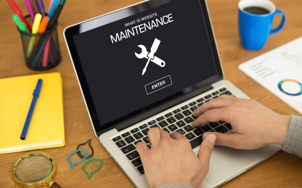 A person typing on a laptop with a screen showing a message about website maintenance, including a wrench and screwdriver icon