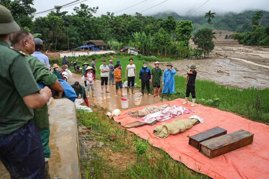 Residents and police officers stand next to victims of a landslide in the remote mountainous village of Lang Nu, in Lao Cai province on September 11, 2024, in the aftermath of Typhoon Yagi hitting nor