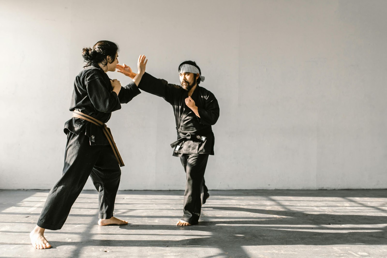 A martial arts instructor teaches a female student how to defend against a strike