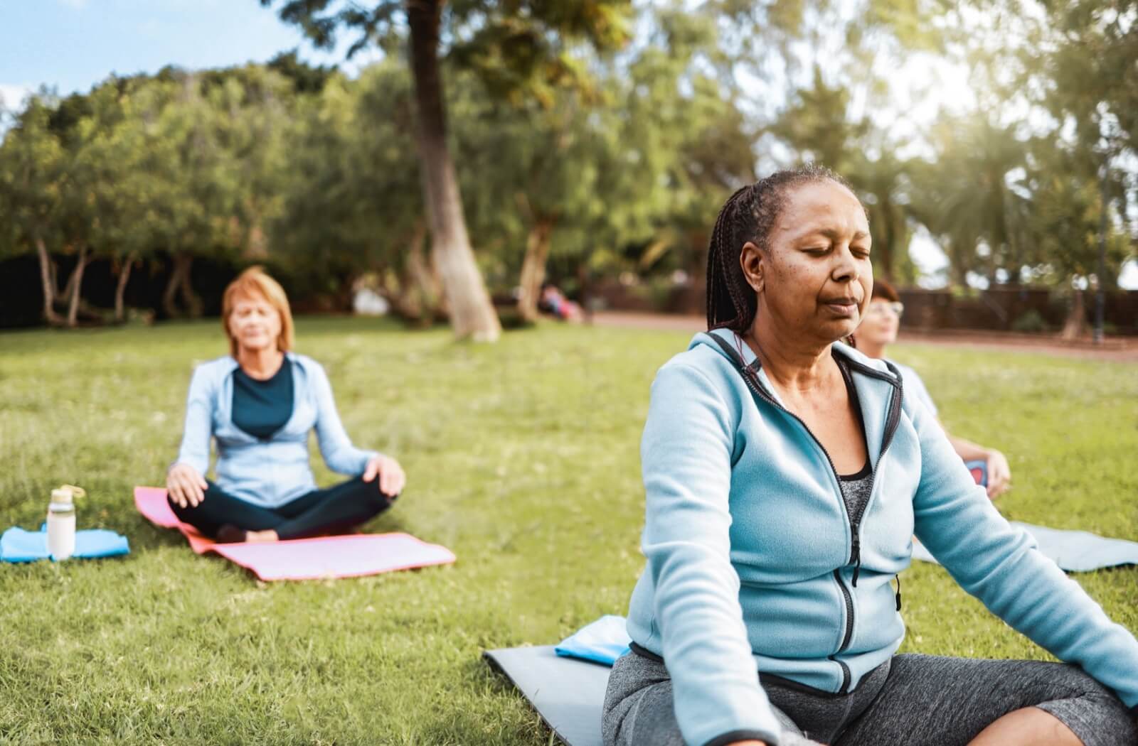 A group of seniors meditate on yoga mats in a sunny park.