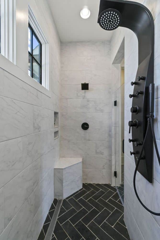 The walk-in shower has marble tiled walls, a corner seat, and matte black fixtures.