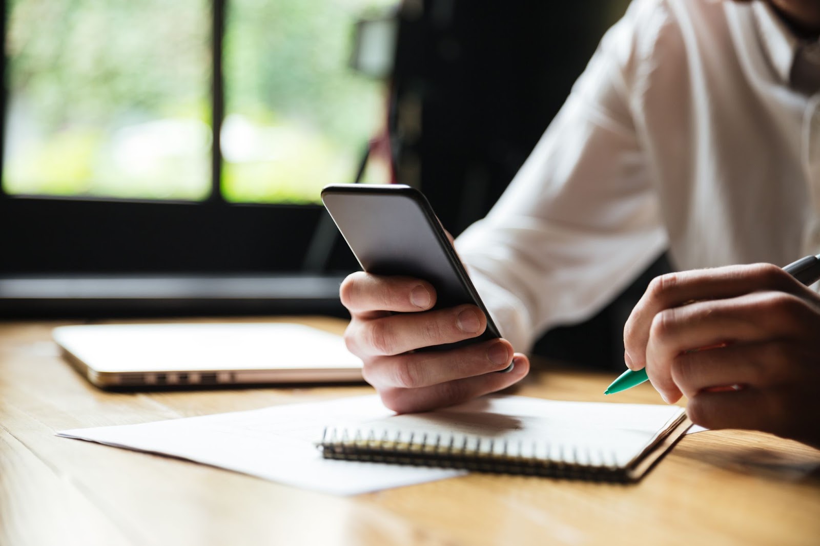 Hombre usando su teléfono móvil mientras escribe en un cuaderno