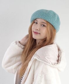 This may contain: a girl with long hair wearing a blue hat and jacket, standing in front of a white wall