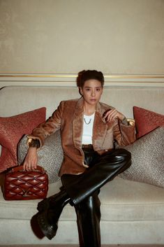 This contain an image of  Amber Liu sitting on top of a white couch holding a brown purse and wearing black leather pants