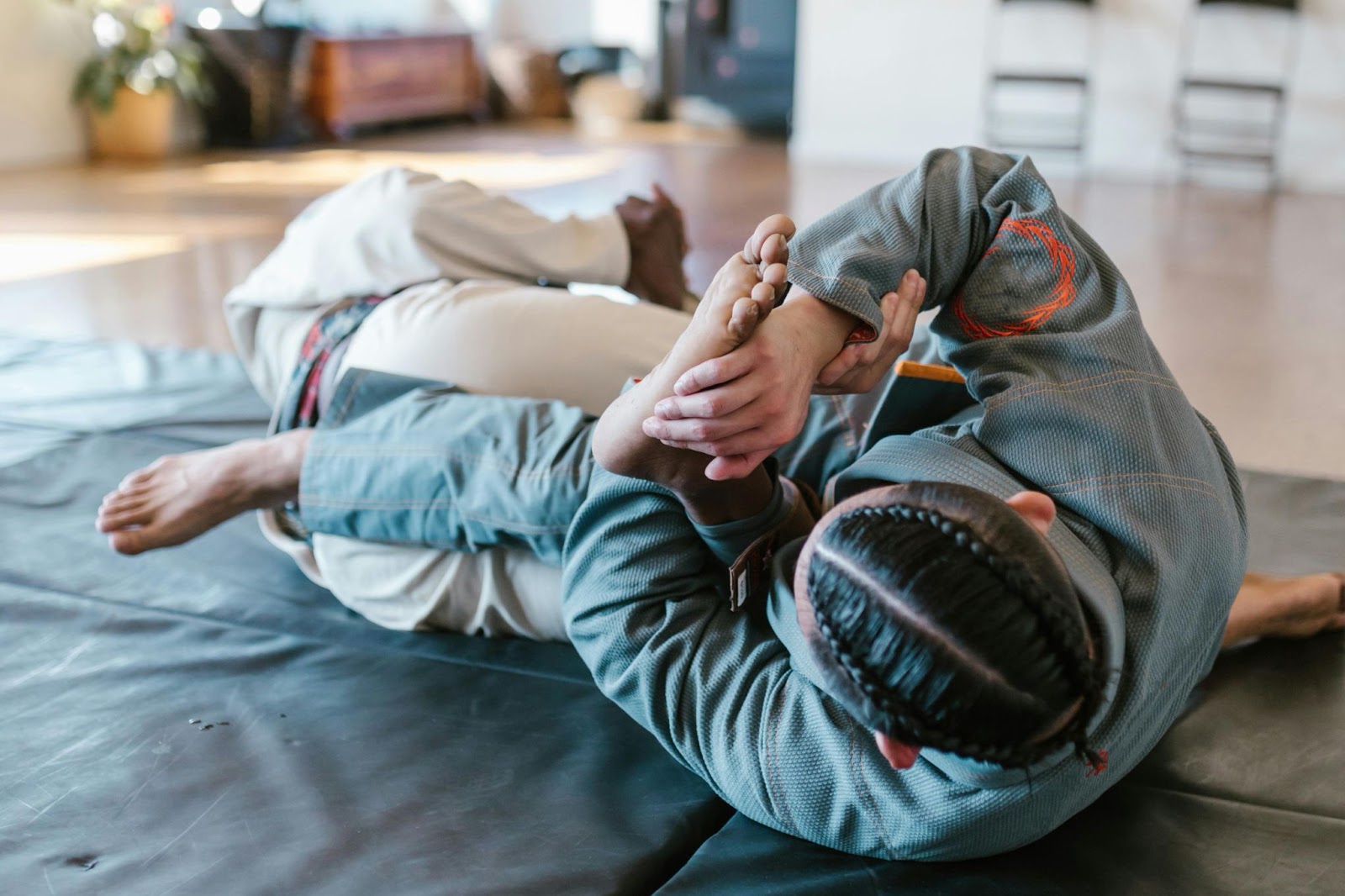 A martial arts student executes a foot lock technique on an instructor lying on the ground during a training session. 