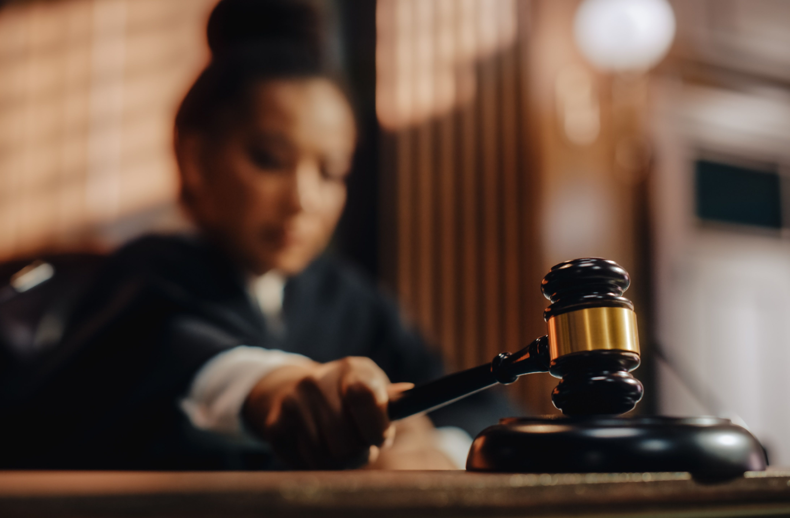 A gold-banded, mahogany gavel is slammed onto a court desk by a blurred judge.