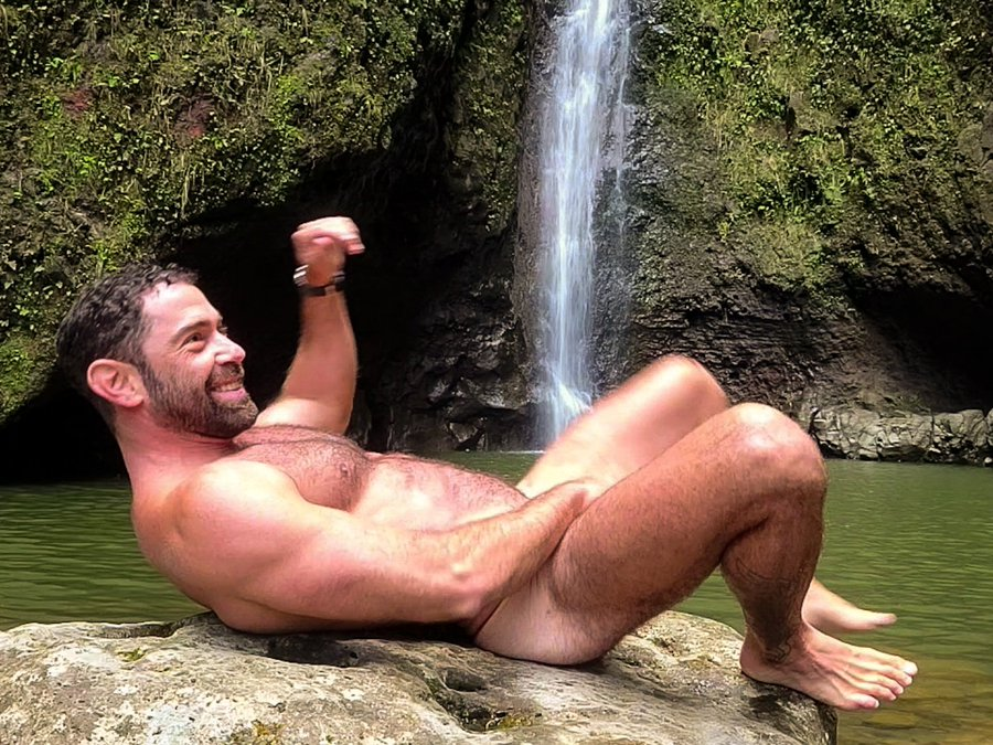 gay xxx onlyfans content creator Roman Mercury naked lying on a rock near a waterfall showing off his hairy chest and gay bubble butt