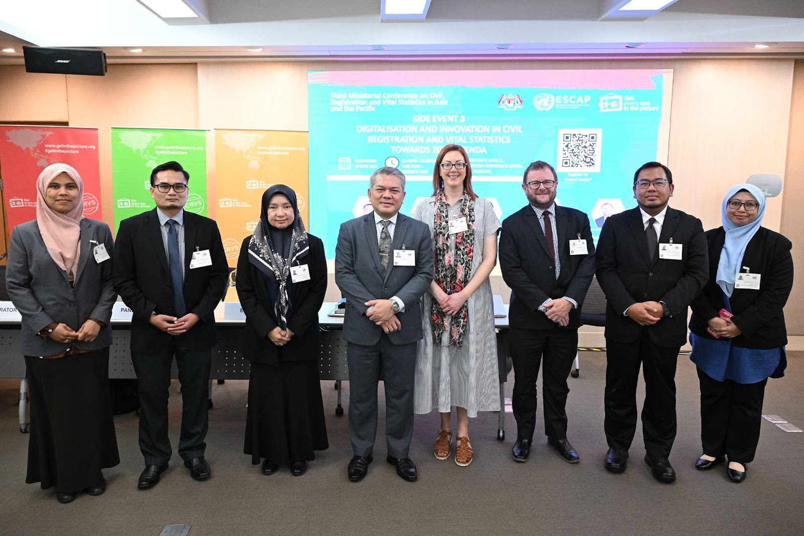 A group of people standing in front of a screenDescription automatically generated