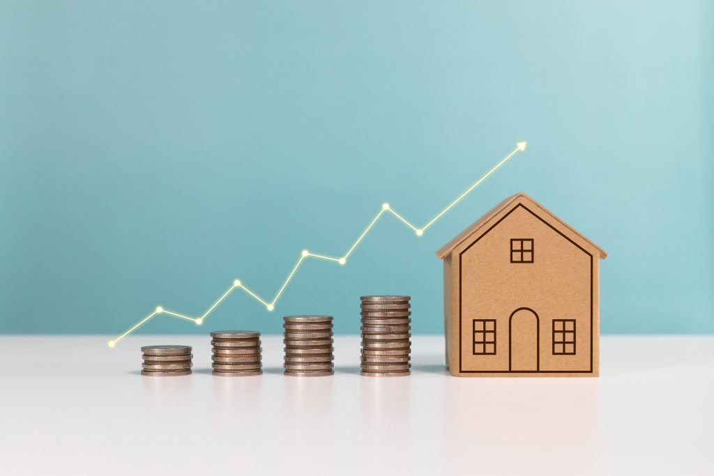 stacks of quarters lined up next to each other in ascending order support a graph line showing the relationship between the money spent when home remodeling projects and their related benefits. next to the quarters is a house representing your dream home.