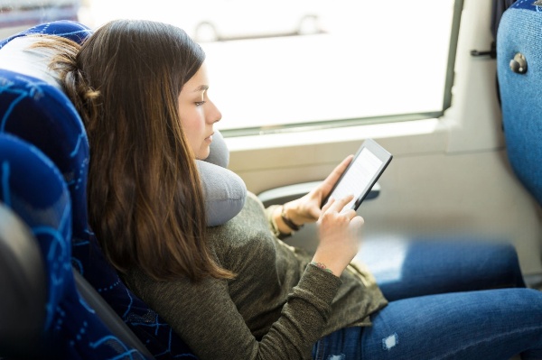 A woman sitting comfortably using a compact travel cervical pillow to support her neck.