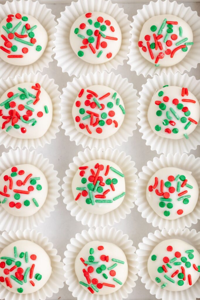 Rows of sugar cookies in paper glasses, each topped with red and green sprinkles.