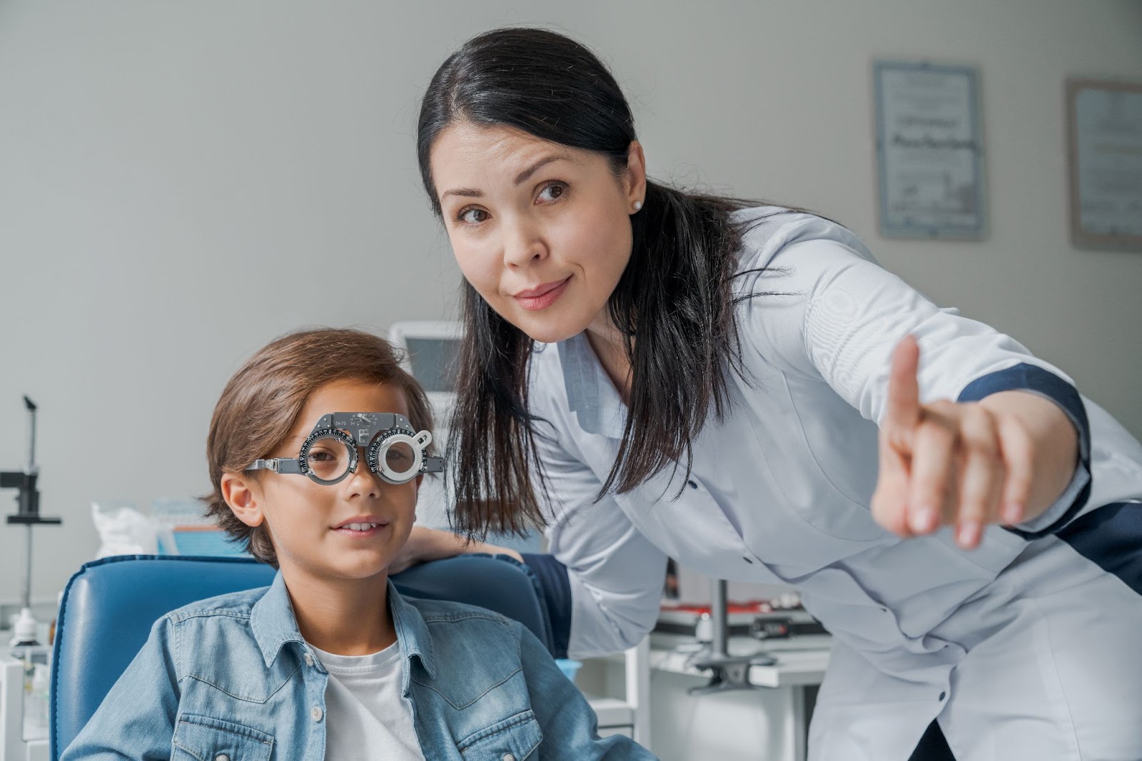 A young boy smiling in an optometry office while a female optometrist tests for myopia.