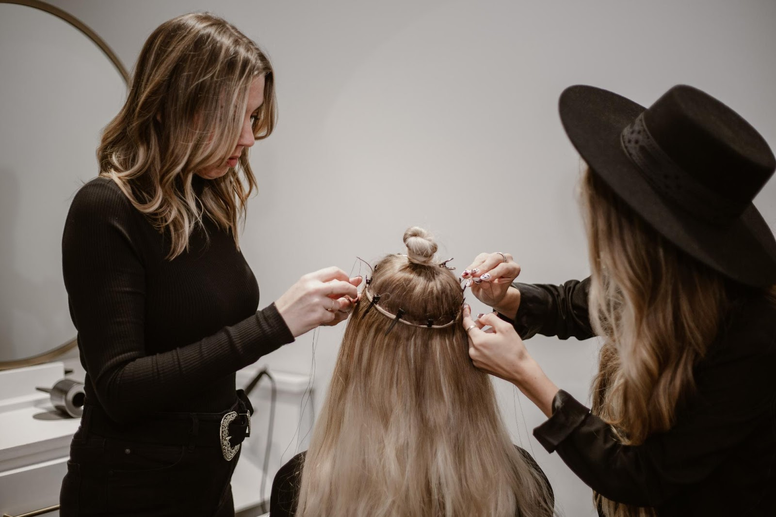 Two stylists installing beaded weft extensions on blonde hair