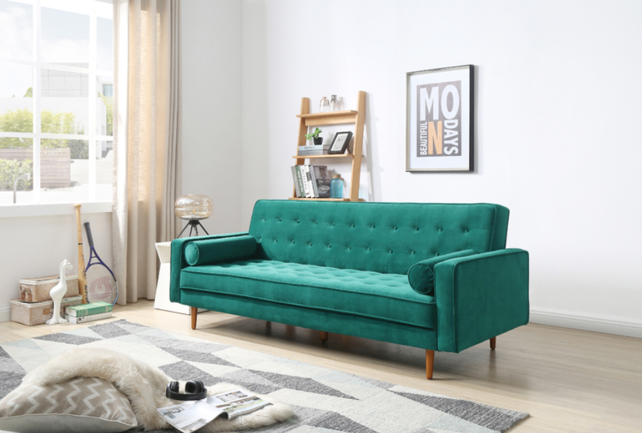 A modern living room featuring home furniture, including a teal-green tufted sofa with wooden legs, set against a bright white wall