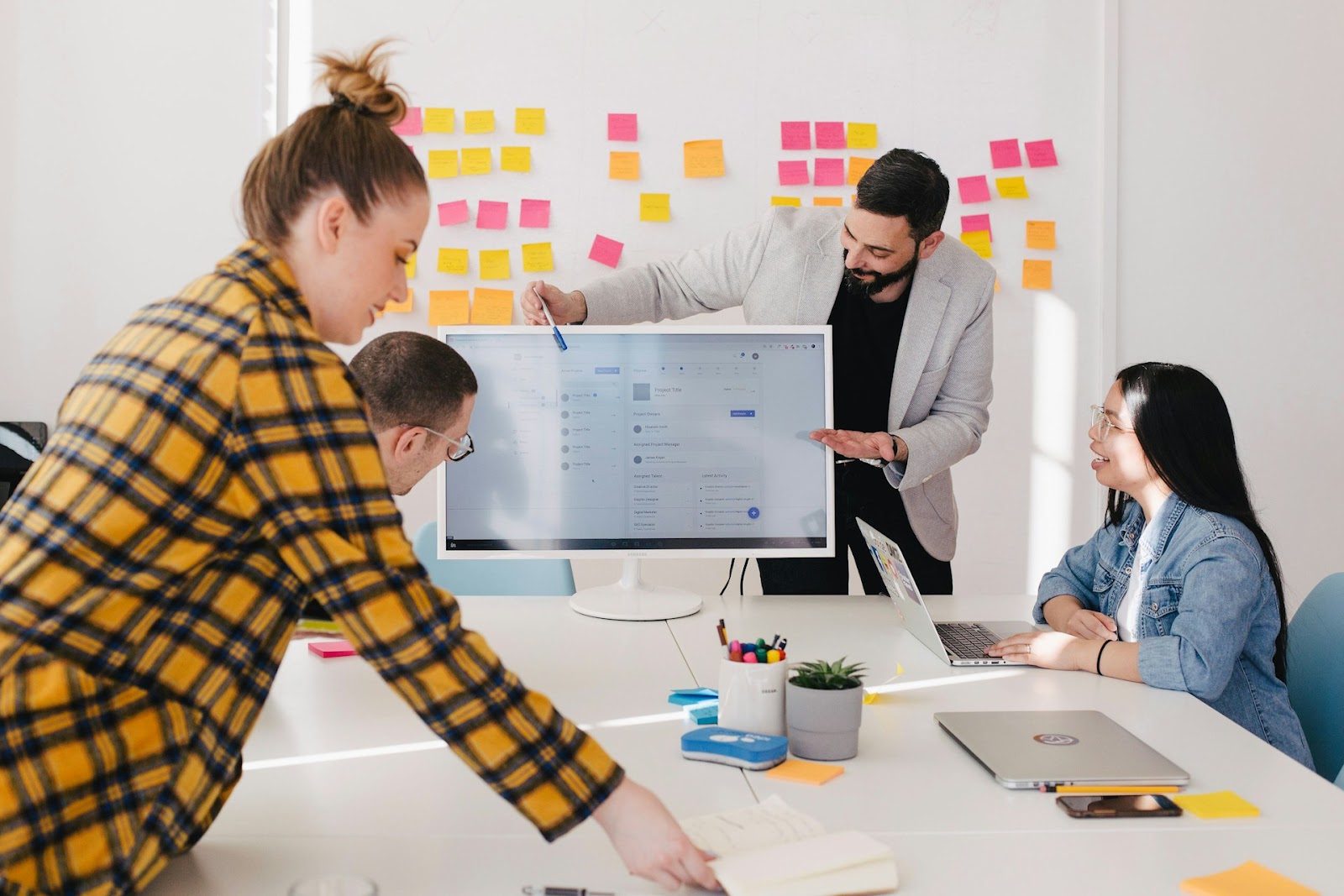 A diverse group of people collaborating in a meeting room, surrounded by colorful sticky notes on the wall.