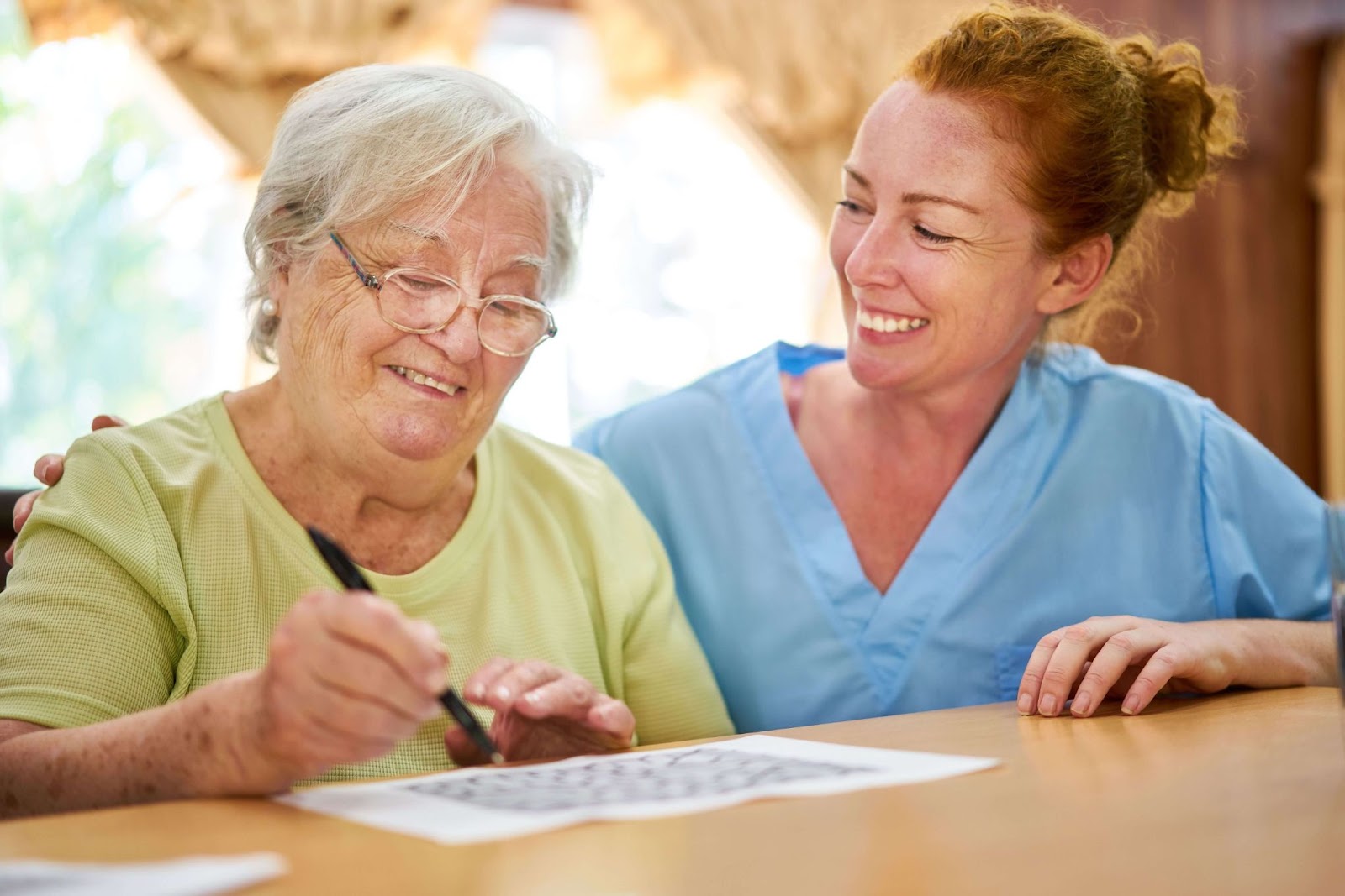 A staff member assisting an older adult with dementia do a puzzle in memory care.