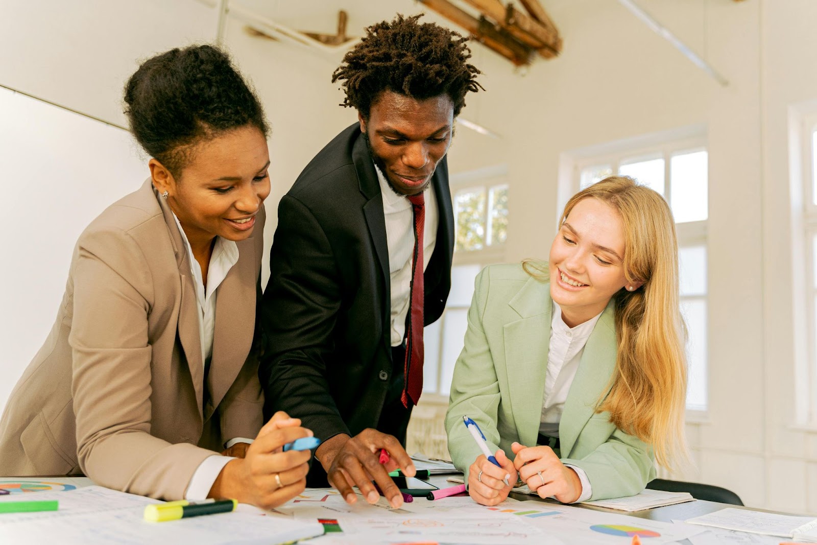 Three people look over artwork during an office meeting at a table.