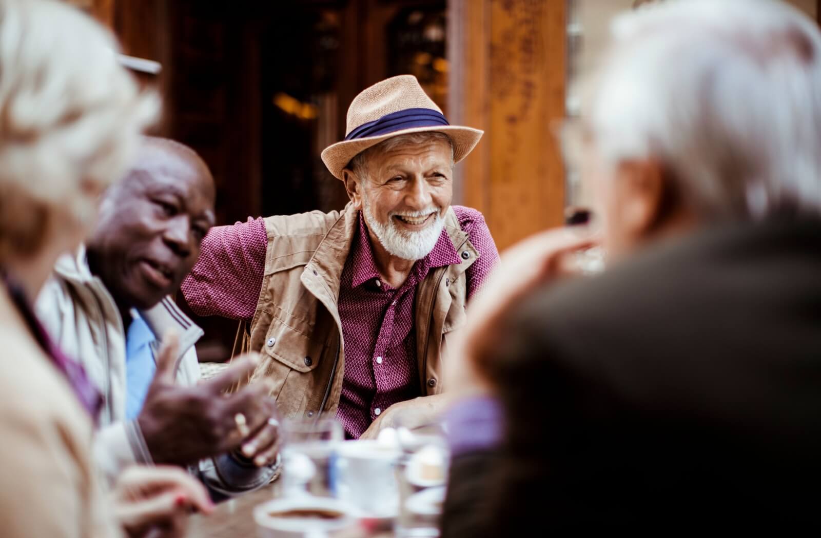 A group of seniors laughing and smiling together over drinks at an outdoor patio