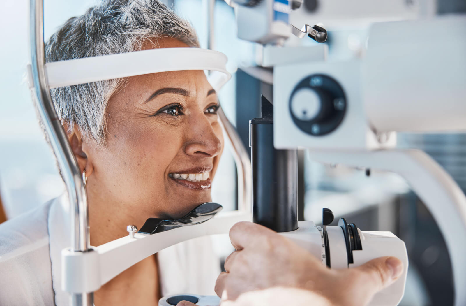 A senior woman smiling during an eye exam while being checked for cataracts.