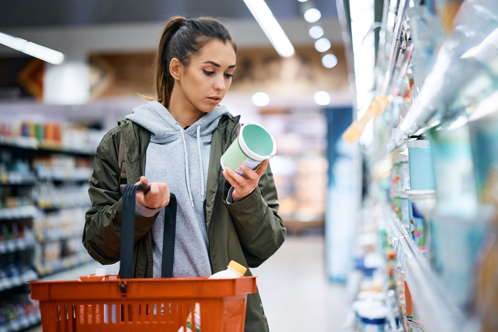 Young woman reading product ingredients in a store to spot potential greenwashing signs.