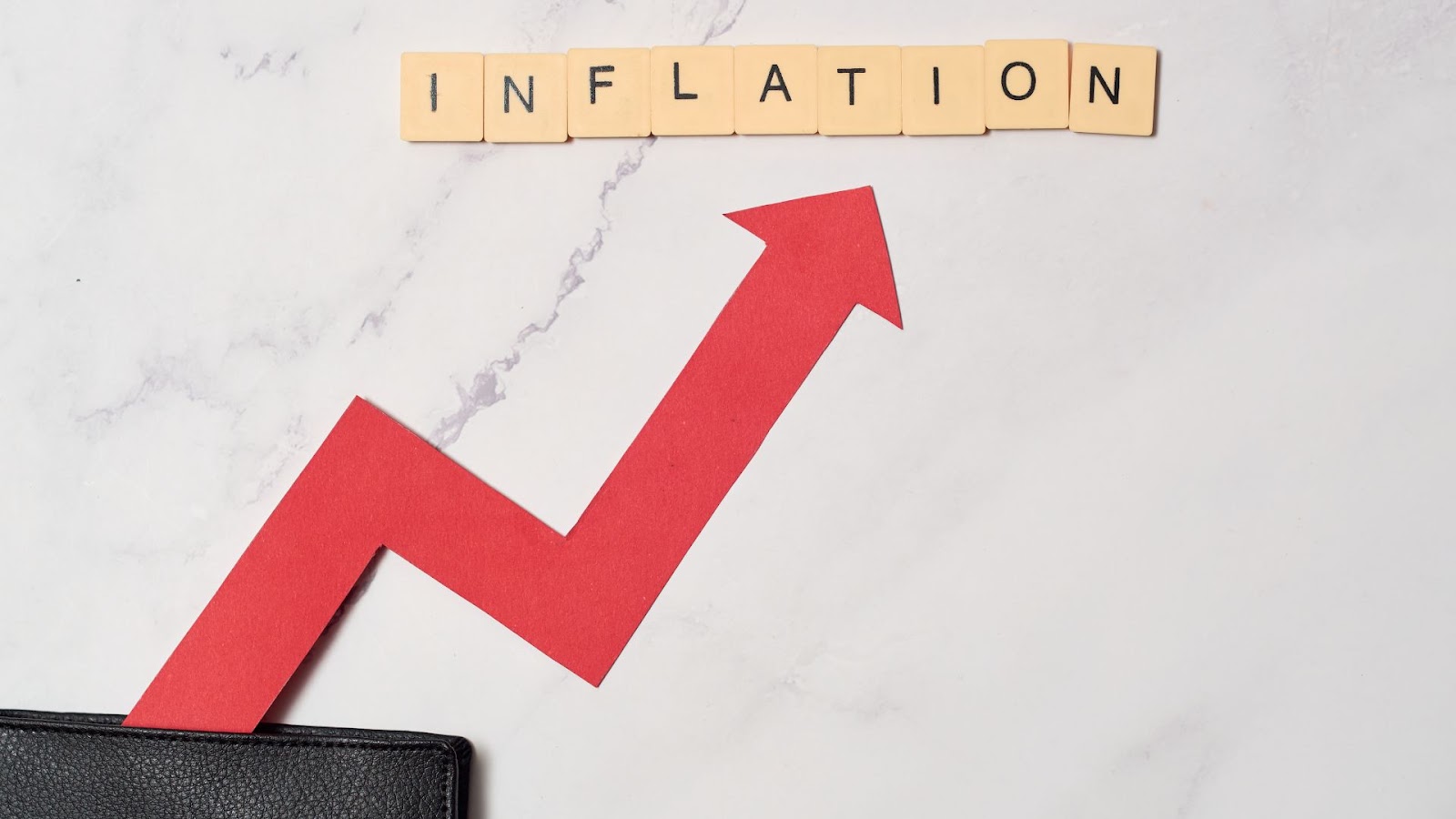 The word inflation is cut out of a wallet with a red arrow pointing to it on a marble surface.