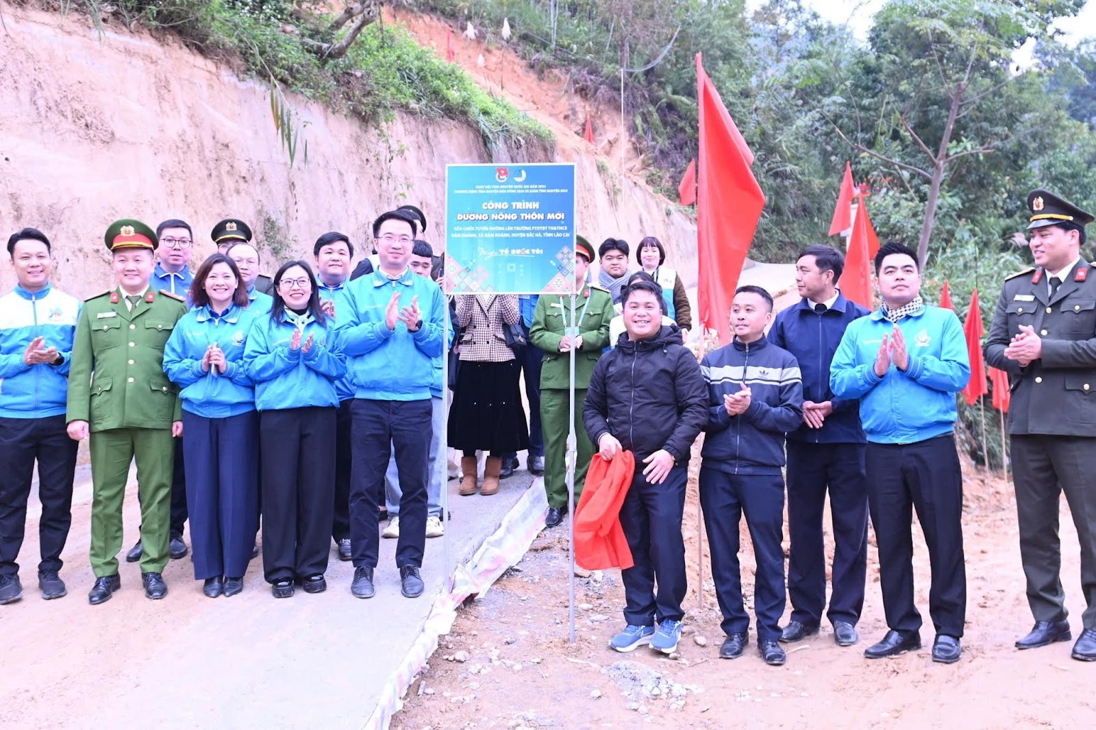 A group of people standing on a road with flagsDescription automatically generated