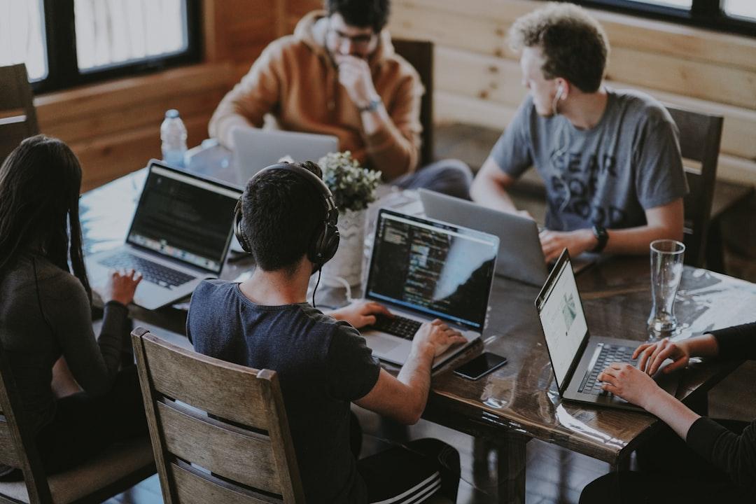 A group of people sitting around a table with laptops<br />
<br />
Description automatically generated