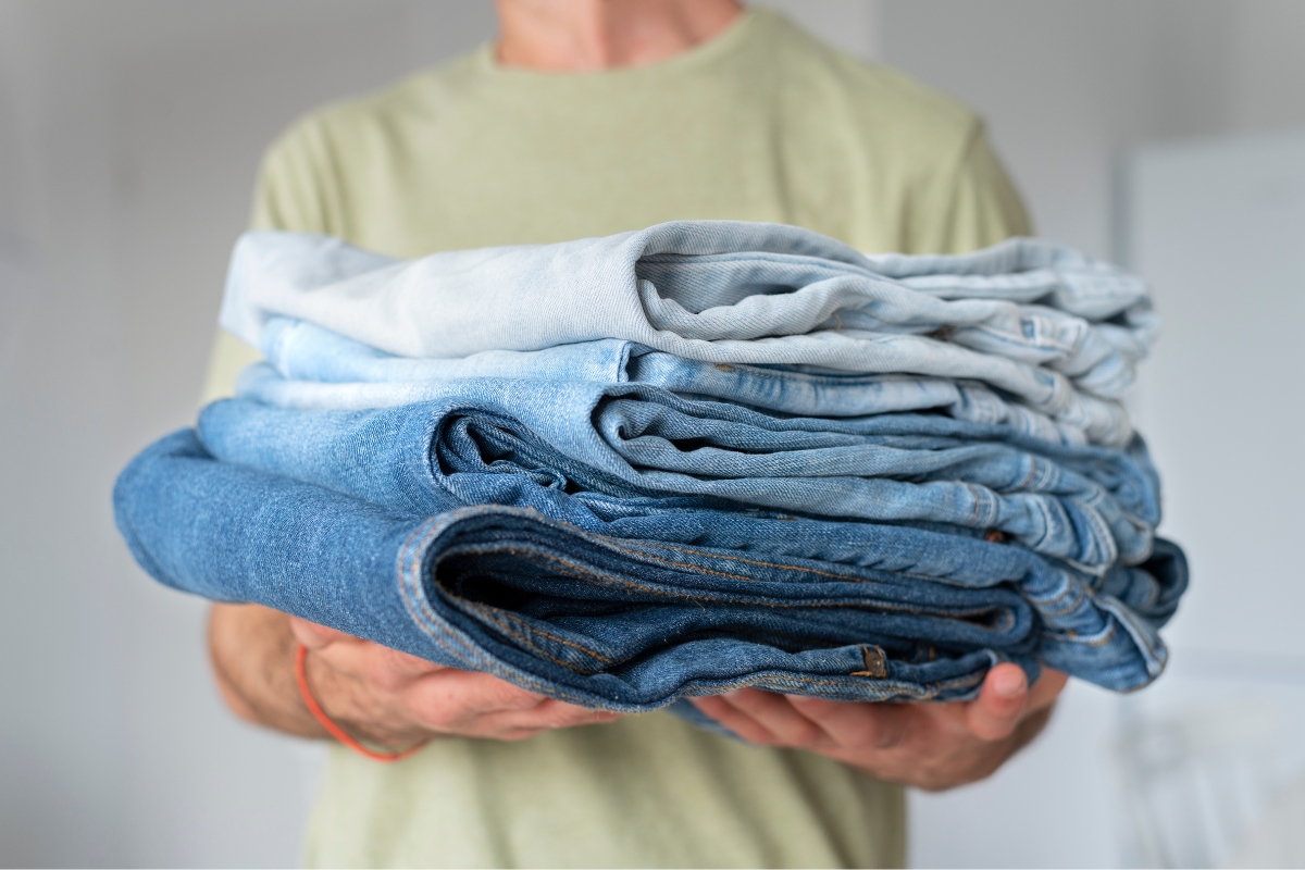 Pria membawa tumpukan celana jeans yang sudah dilipat.