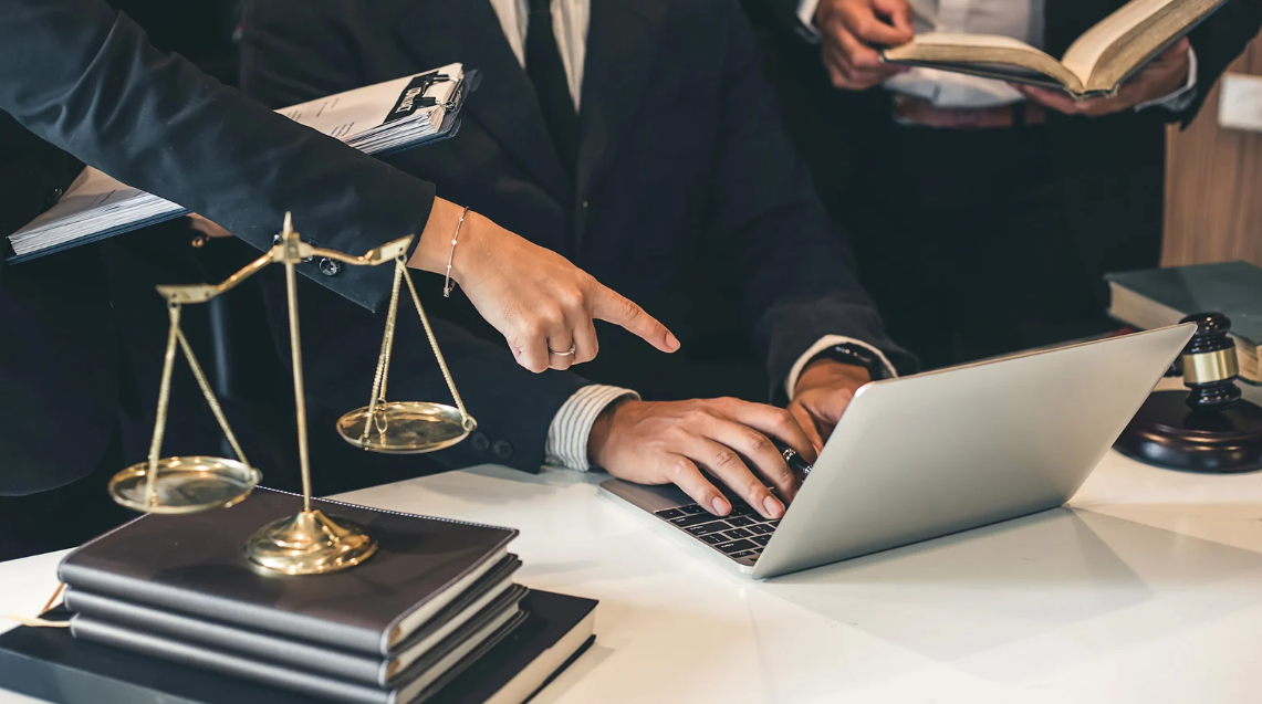 (Legal team working collaboratively at a desk with law books, a scale of justice, and a laptop—symbolizing research, strategy, and pursuit of justice.)