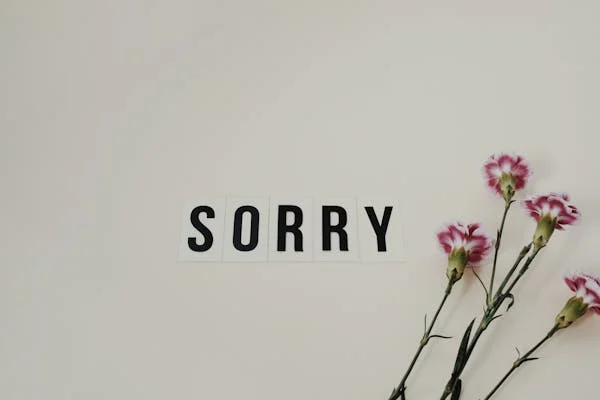 The word 'Sorry' written beside some flowers on a white surface, symbolizing an apology for delays