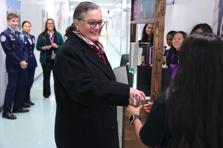 Dr. Reid being handed a cup of a coffee by a student in a school. 