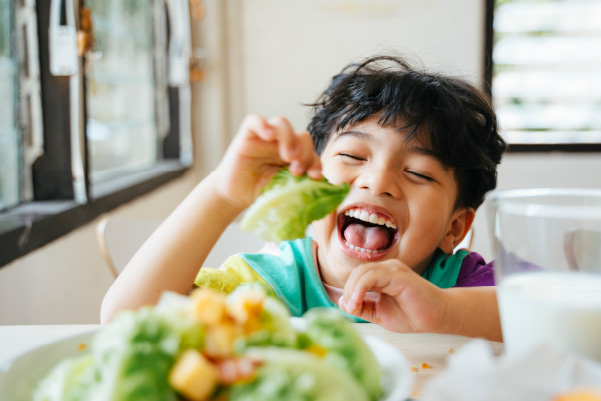 A boy happily eating vegetables and supporting balanced diet chart for a 10 years old.
