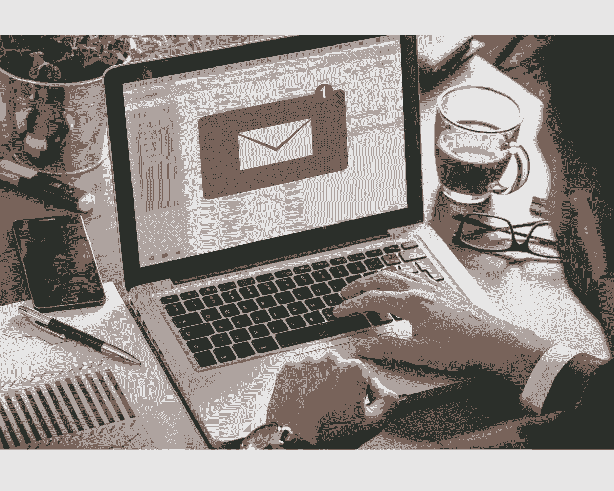 A person working on a laptop with an email notification icon displayed on the screen. The laptop is on a desk with a cup of coffee, a smartphone, and some documents nearby. The scene captures a typical work environment with a focus on real-time email notifications.