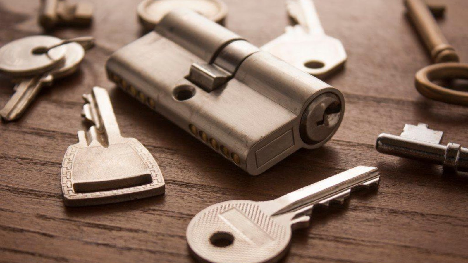 A lock cylinder and keys displayed on a wooden surface for rekeying