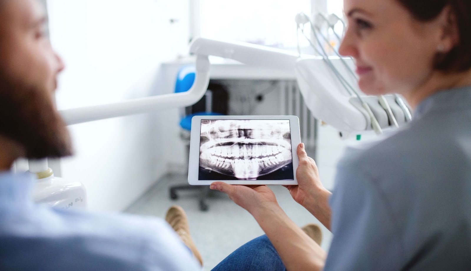 A dentist explaining a dental procedure to a patient while holding a dental X-ray image.