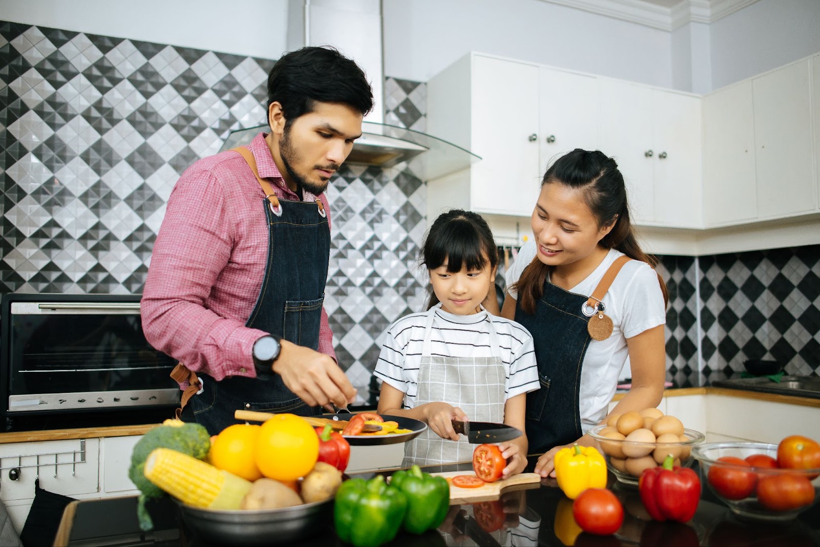 seorang pria dan wanita sedang memasak bersama anak mereka di dapur yang ceria dan penuh kebahagiaan.