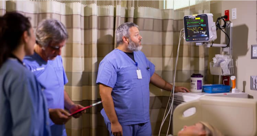 Three medical staff members in scrubs standing in a patient's room