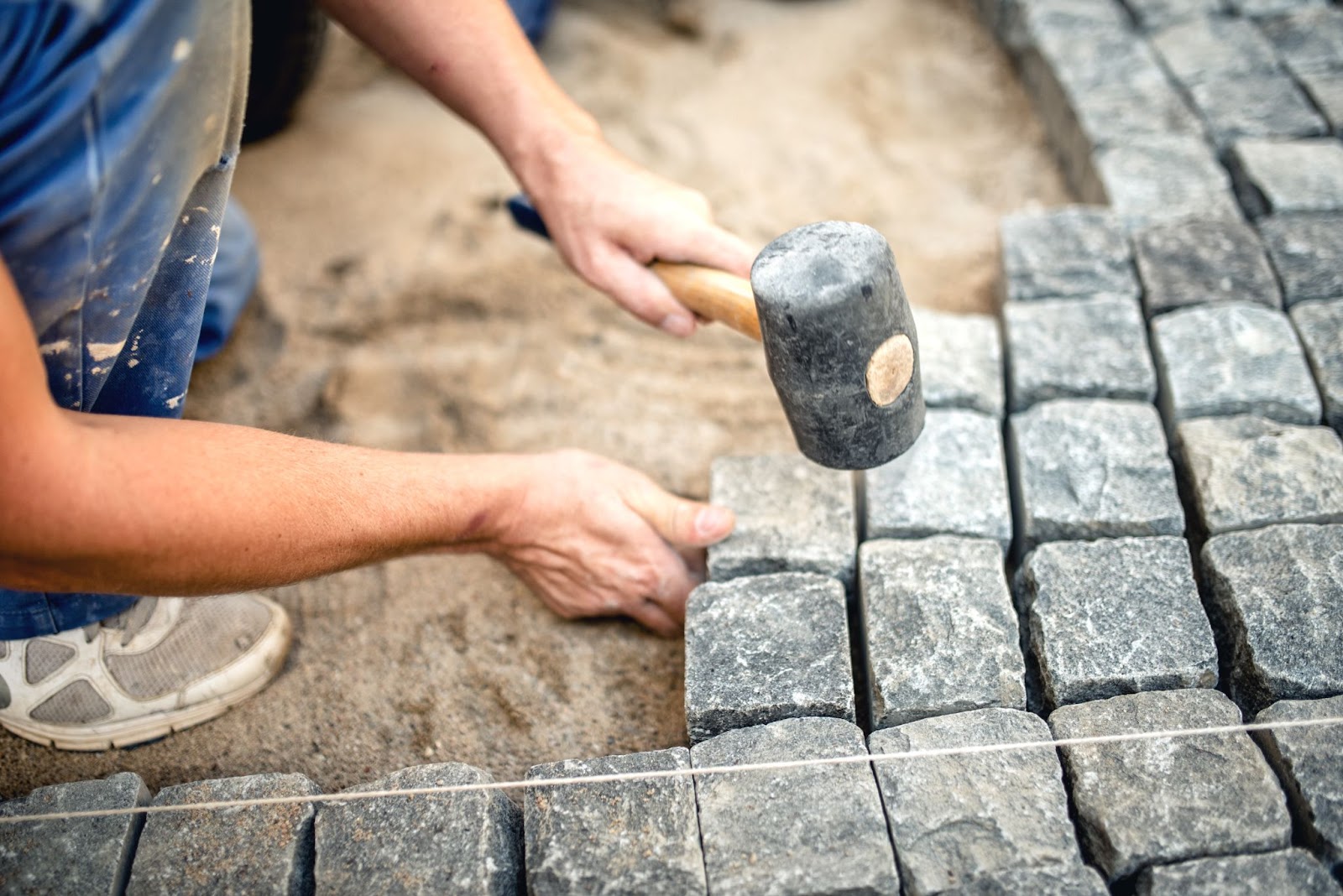 A worker installs cobble and granite stones on the pavement.