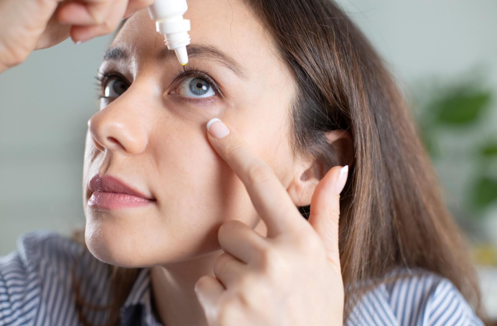 A young adult instill eye drops into their eye to keep them feeling fresh and comfortable.
