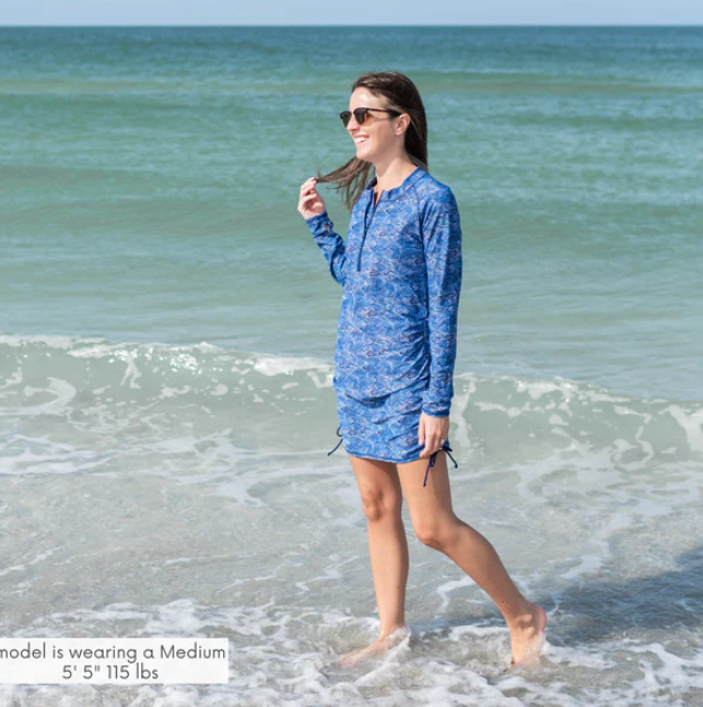 A woman in the ocean in her blue SwimZip postpartum half-zip swim dress—Cute modest bathing suits for coverage and style
