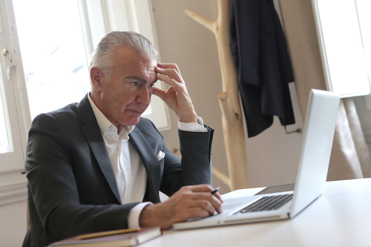 A senior man in a suit sits at a desk, focused on his laptop, exuding professionalism and experience.