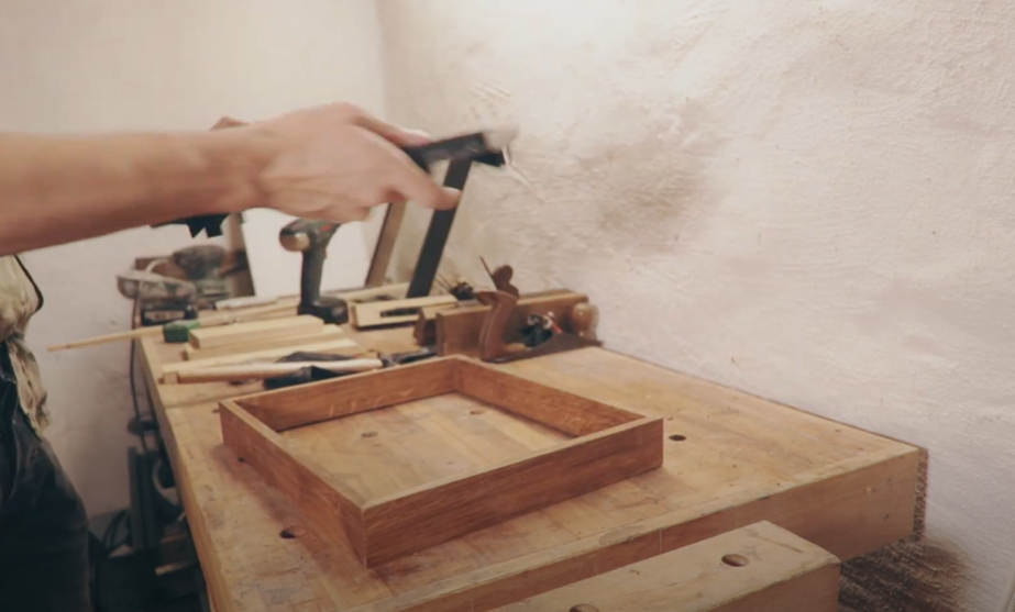 A person working on a wooden frame with tools on a workbench.