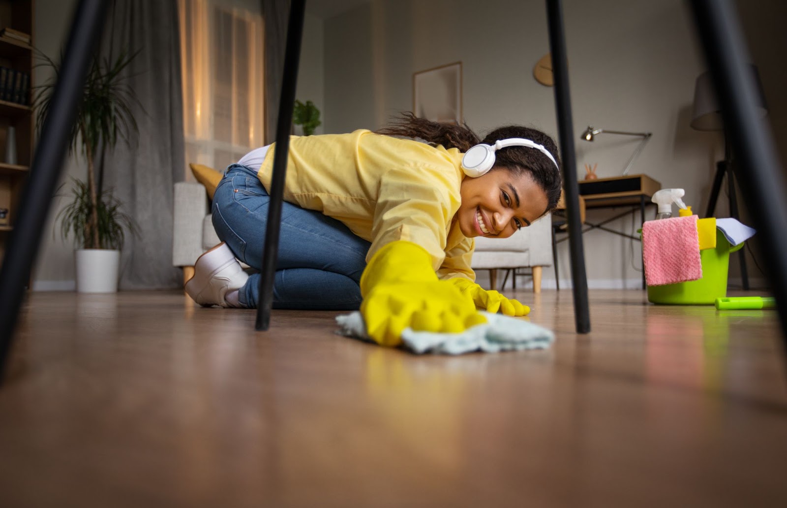 Woman wearing gloves and headphones cleaning a wood floor. 