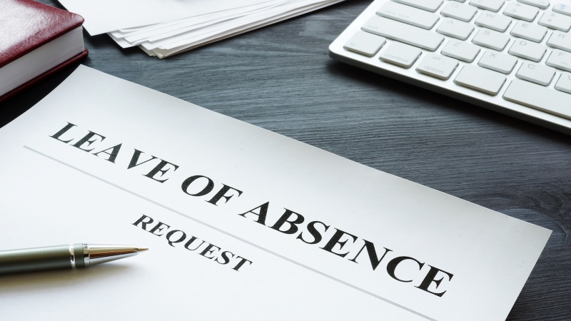 Close-up of a leave of absence request form on a desk with paperwork, a keyboard, and a pen