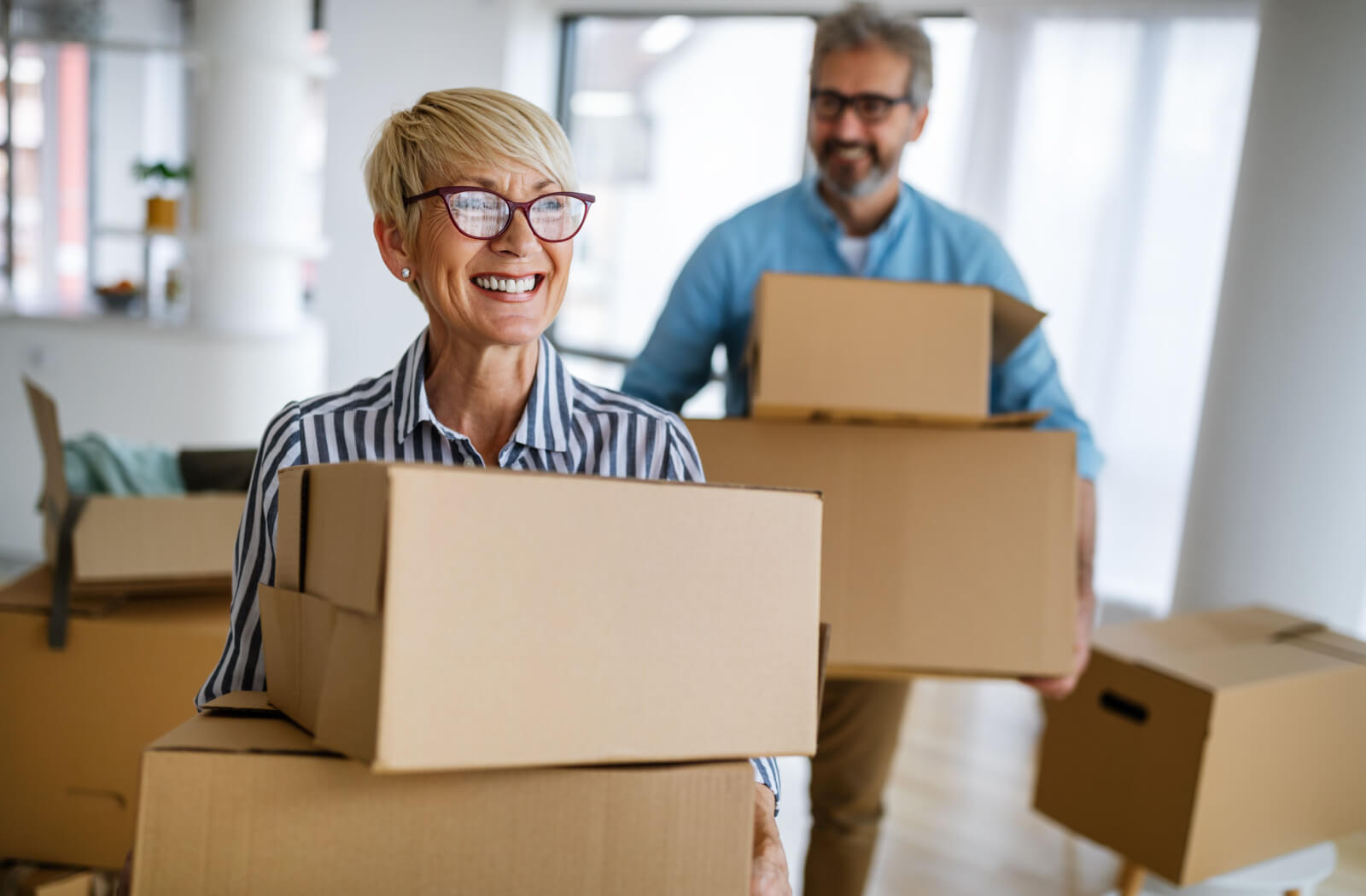 An older couple carrying moving boxes out of their home while downsizing and preparing to move to assisted living.